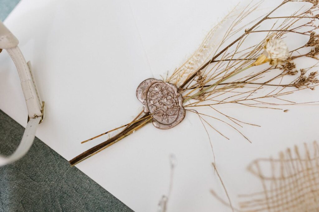 A delicate flat lay featuring dry flowers and a wax seal on white paper, perfect for invitations.